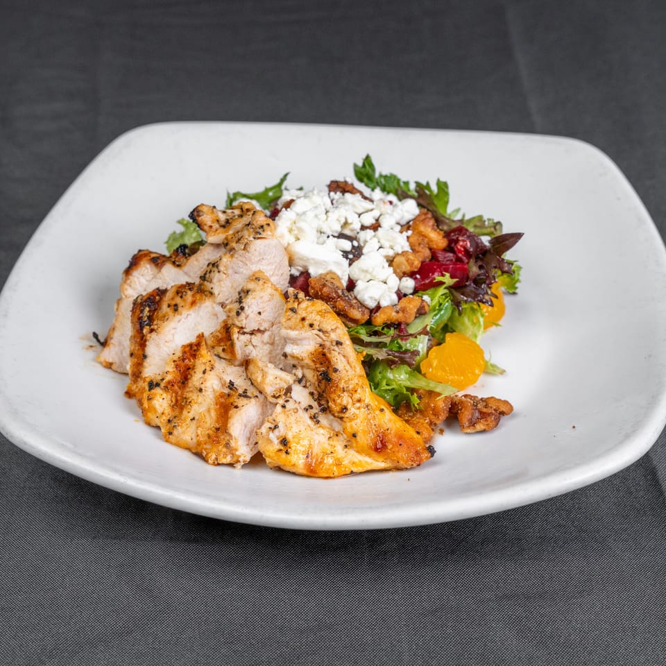 Grilled chicken breast served over mixed greens with feta, cranberries, crispy toppings, and mandarin orange slices on a white plate.