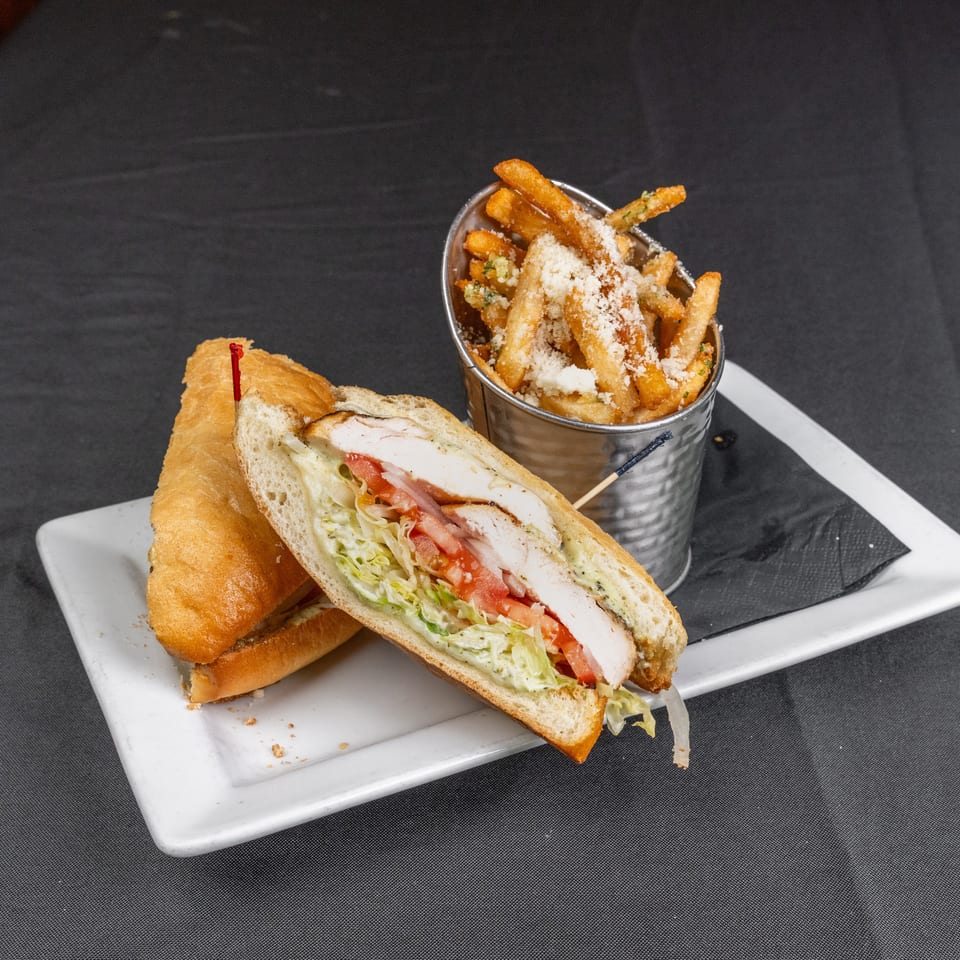 Turkey club sandwich with lettuce, tomato, and bacon served alongside Parmesan-topped fries on a white plate.